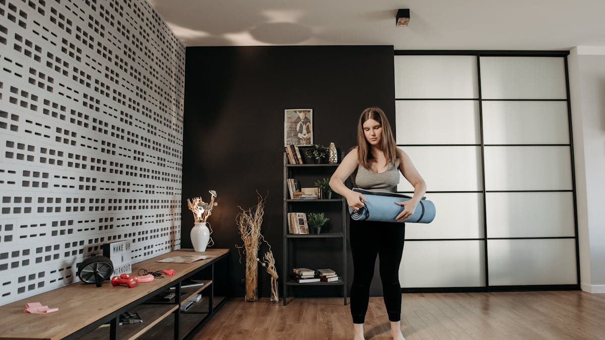 Plus size woman rolling a yoga mat in a stylish indoor setting with modern decor.